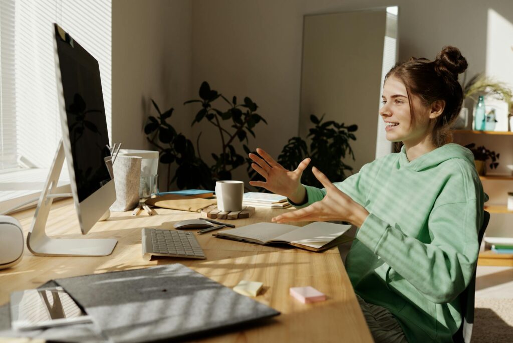 a woman in green hoodie sitting near the table while having conversation through her desktop